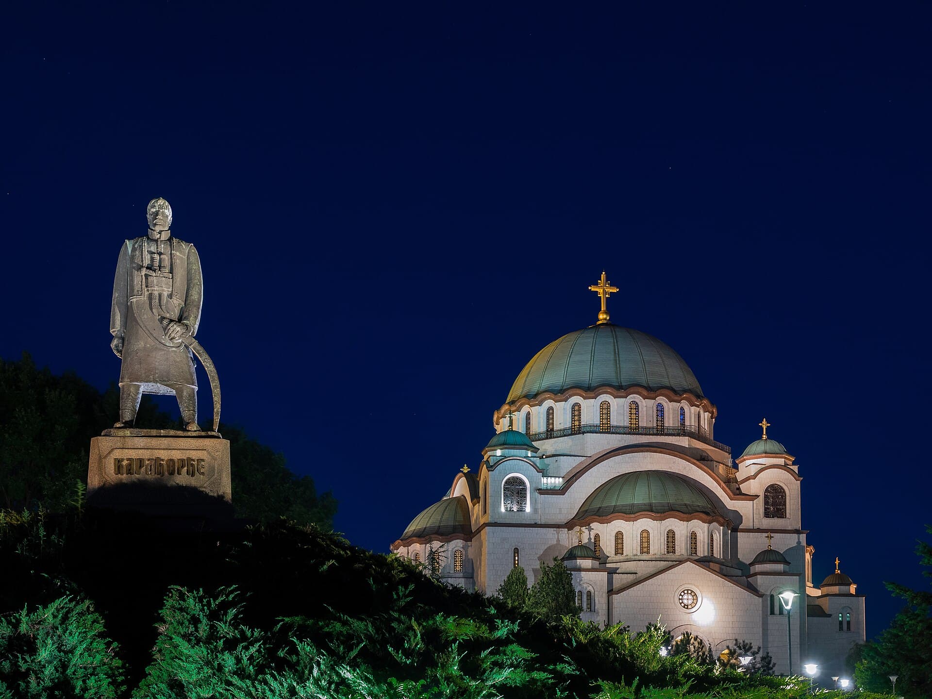The Church of Saint Sava floodlit at night, beside the monument to Karađorđe.