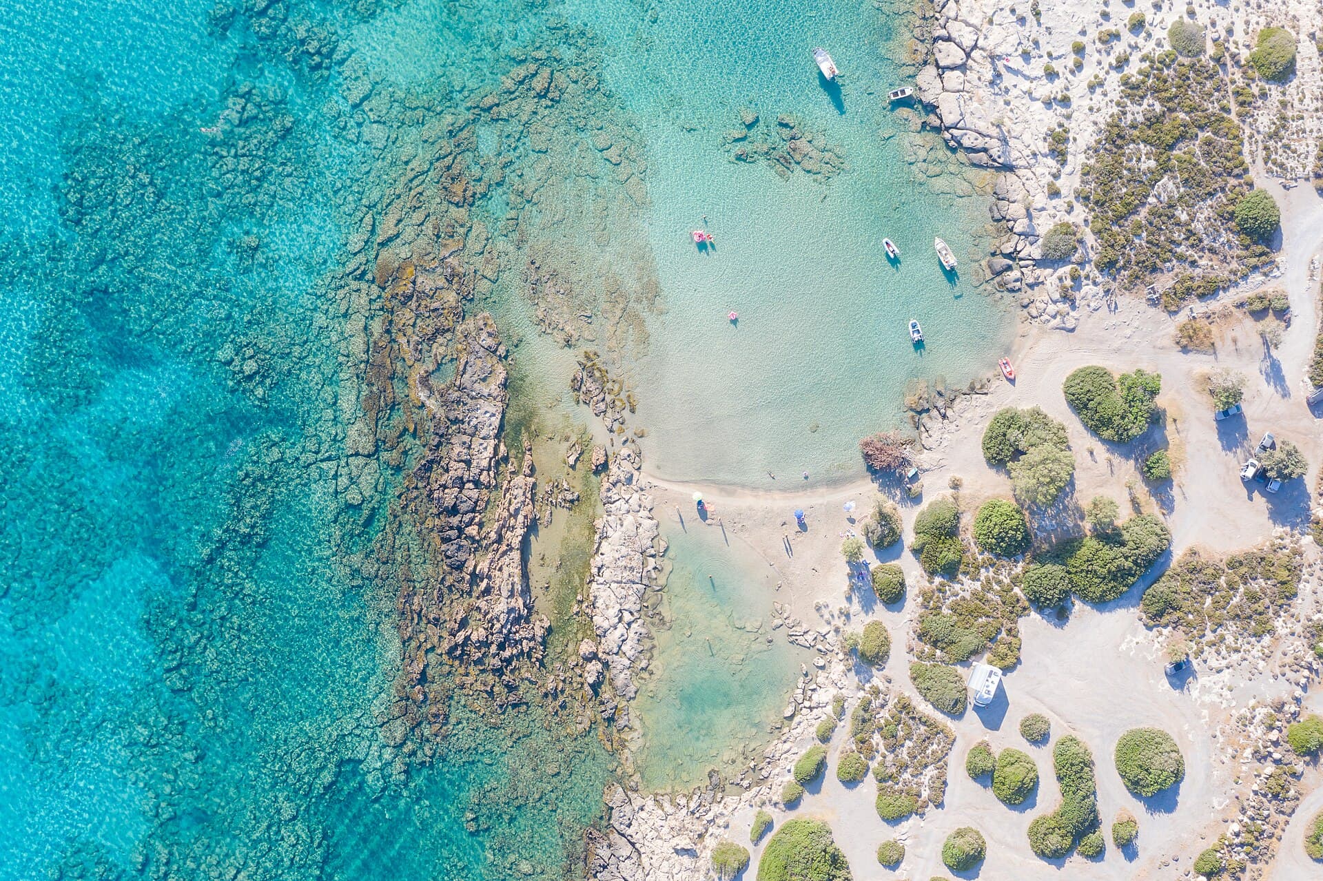Elafonissi dall'alto: l'acqua bassa e turchese tra la spiaggia e l'isolotto, con la celebre sabbia rosata da non portare via.
